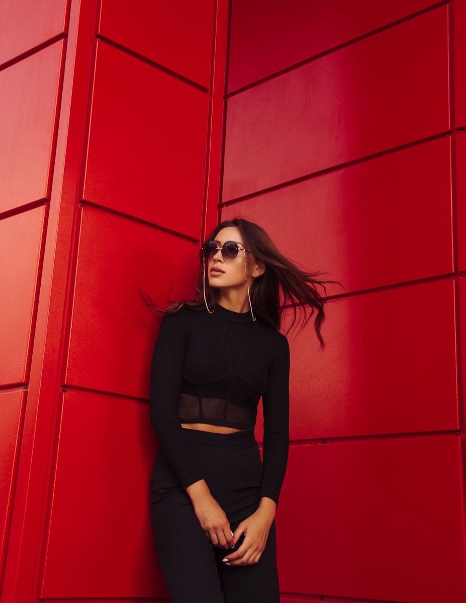 woman in black long sleeve shirt and black pants standing beside red wall